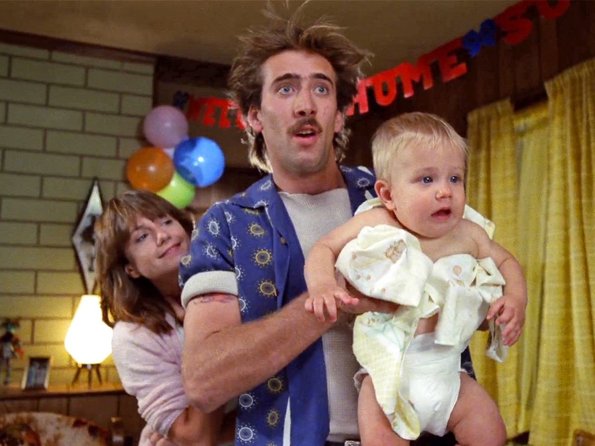 Nicolas Cage holding a blond baby with Holly Hunter behind him