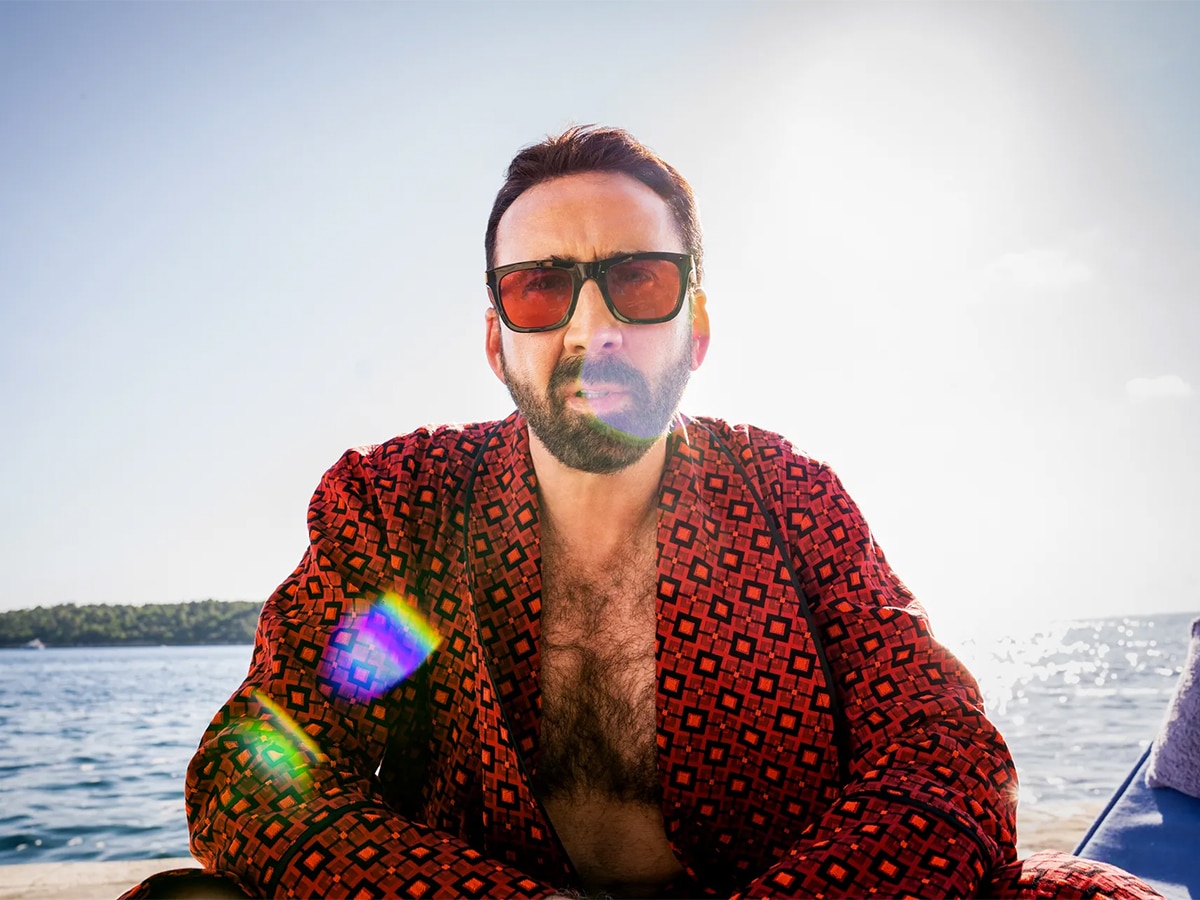 Medium shot of Nicolas Cage wearing red sunglasses and a red patterned robe exposing his chest