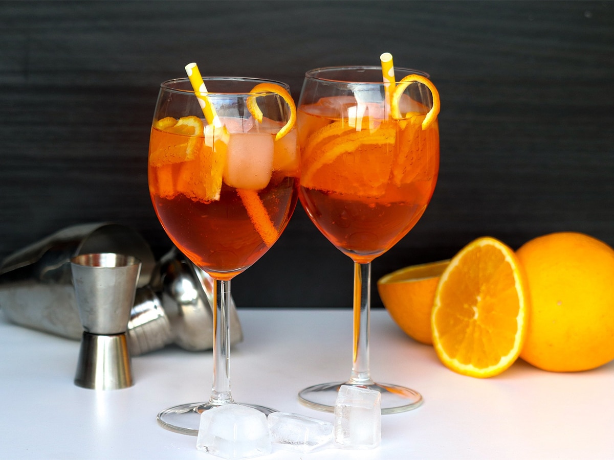 Two glasses of Aperol spritz on the rocks with orange slices set on a white bar with a dark background
