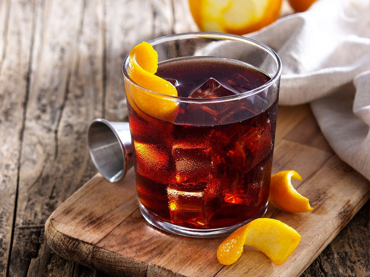 Boulevardier cocktail on the rocks and orange zest on wooden table