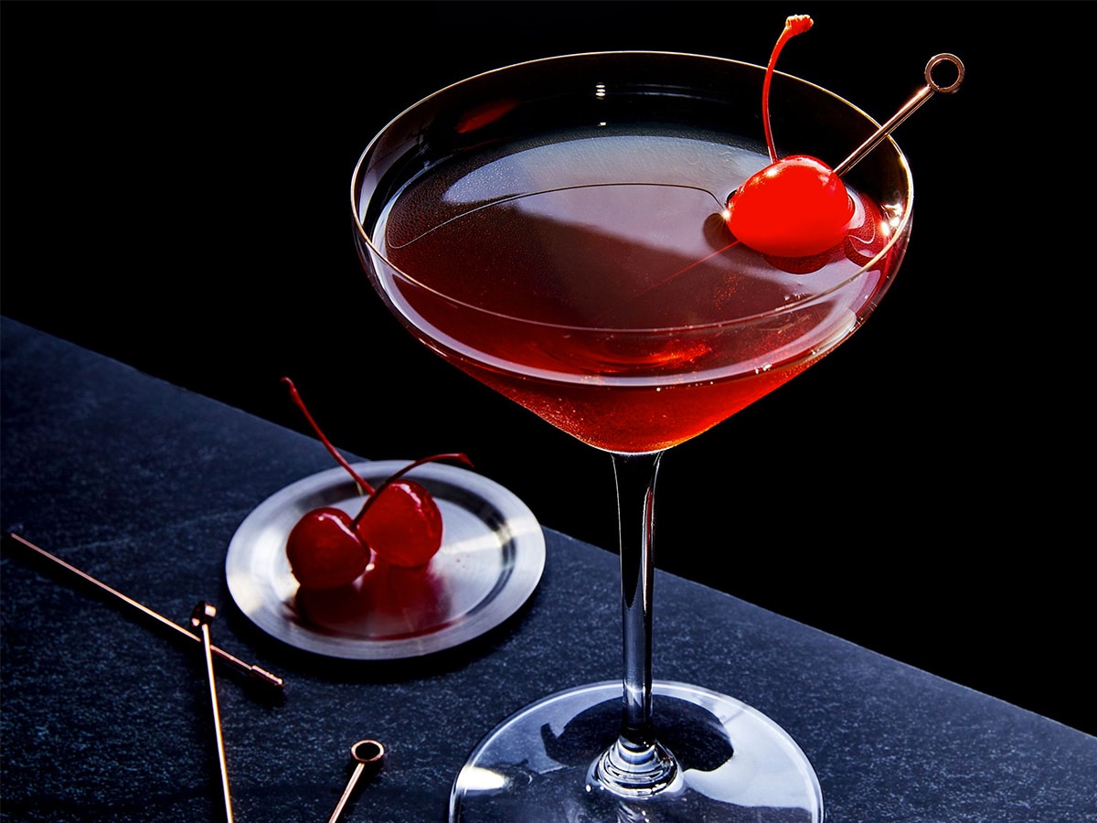 Glass of Manhattan served with a cherry set on a dark tiled bar