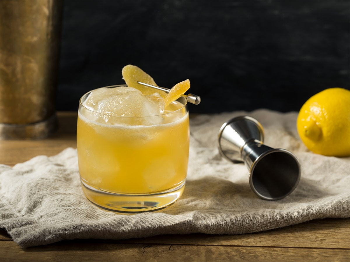 Glass of penicillin cocktail on the rocks with scotch and candied ginger set on a cloth on a wooden bar with a dark background