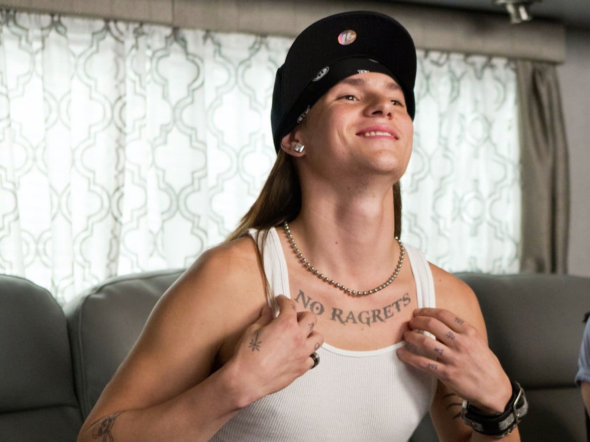 Mark L. Young showing off his lettering tattoo of the words 'NO RAGRETS' below his collarbone