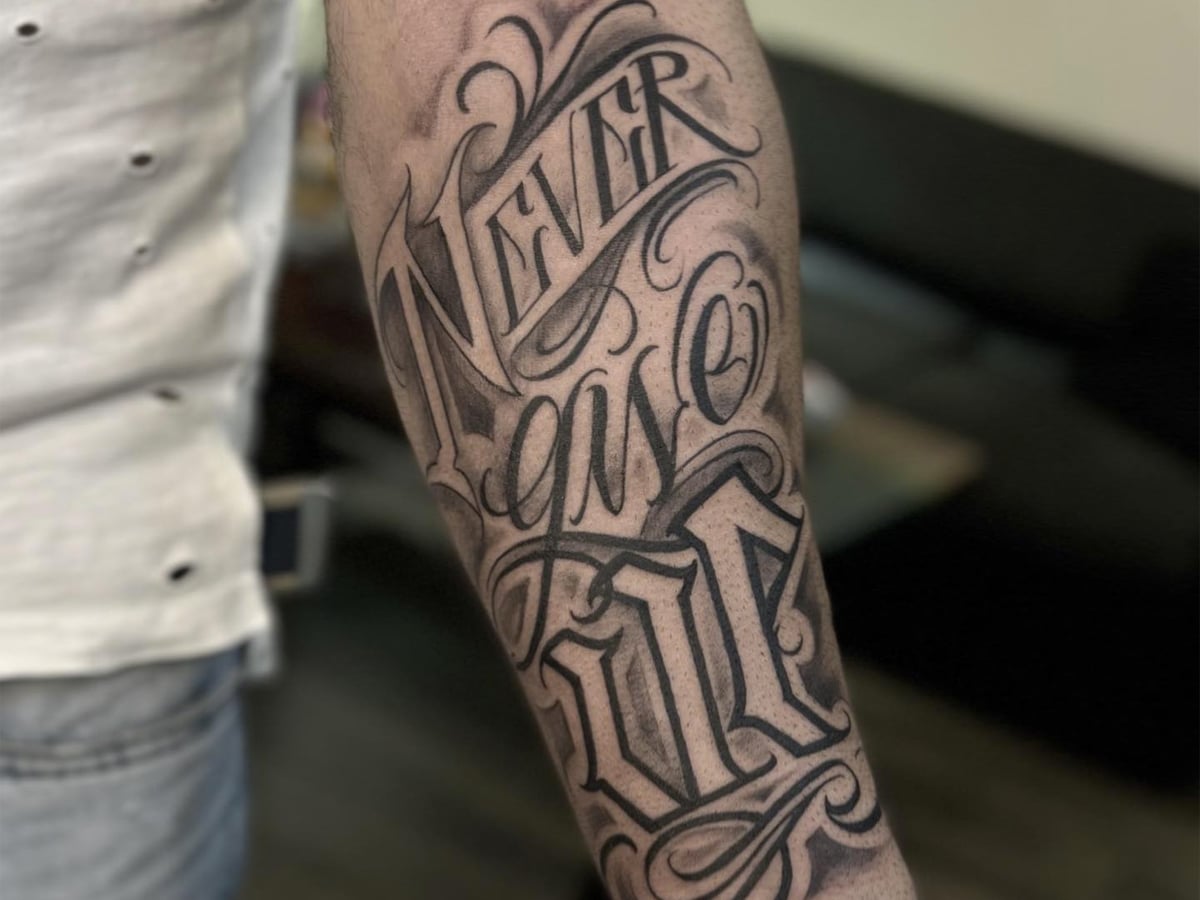 Black and gray lettering tattoo of the words 'Never give up' on a man's arm