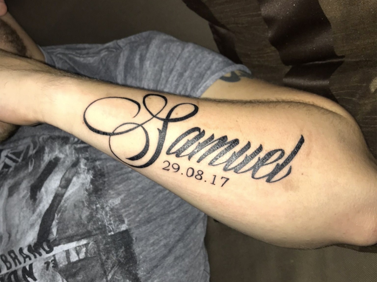 Solid black lettering tattoo of the name 'Samuel' with the date '29.08.17' below