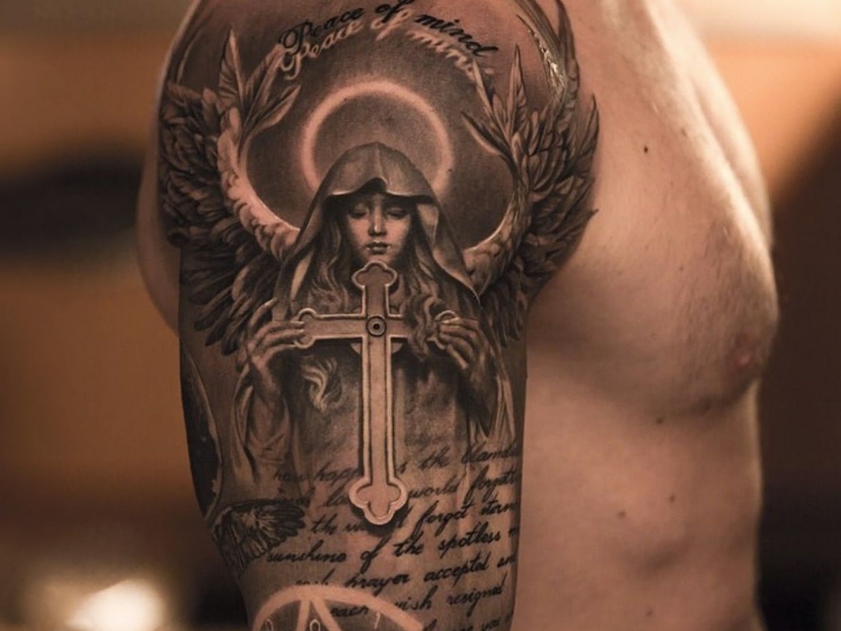 Black and gray tattoo of an angel holding a cross on a man's arm