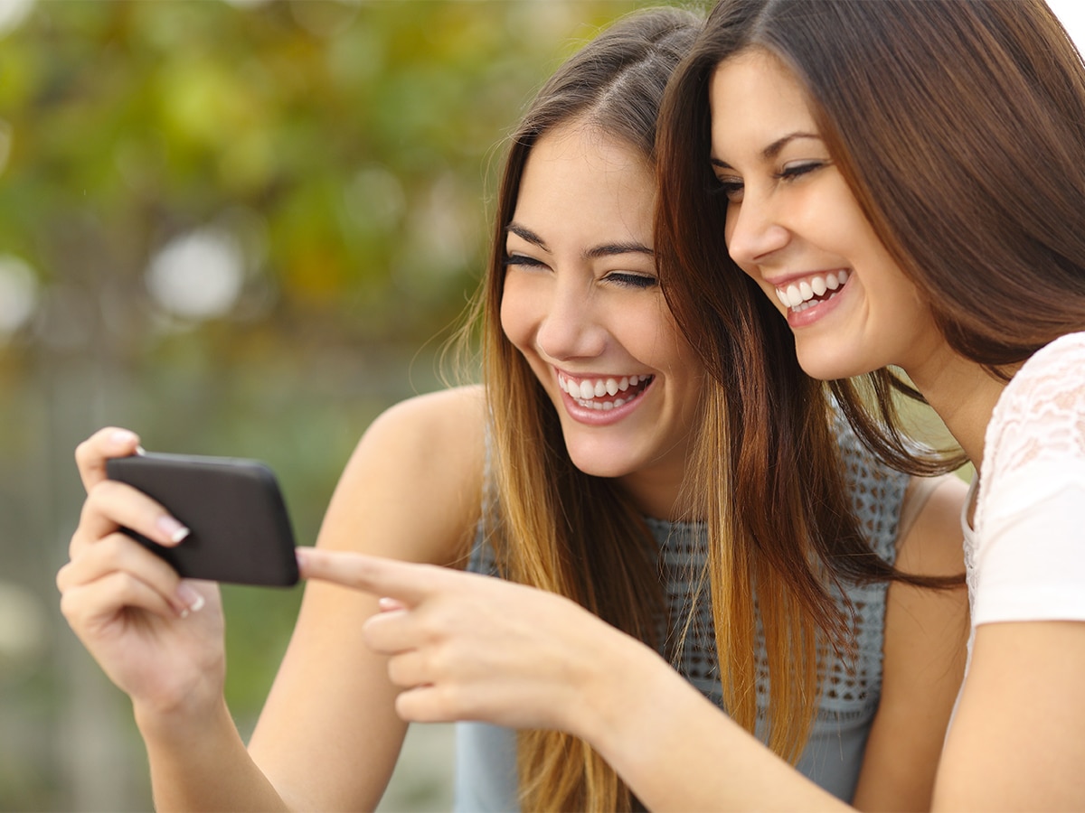 Two women friends laughing while looking at a smart phone outdoors