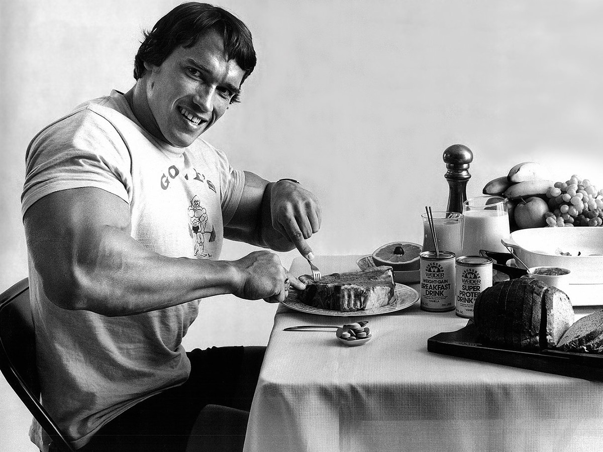 Arnold Schwarzenegger cutting his food with a knife and fork