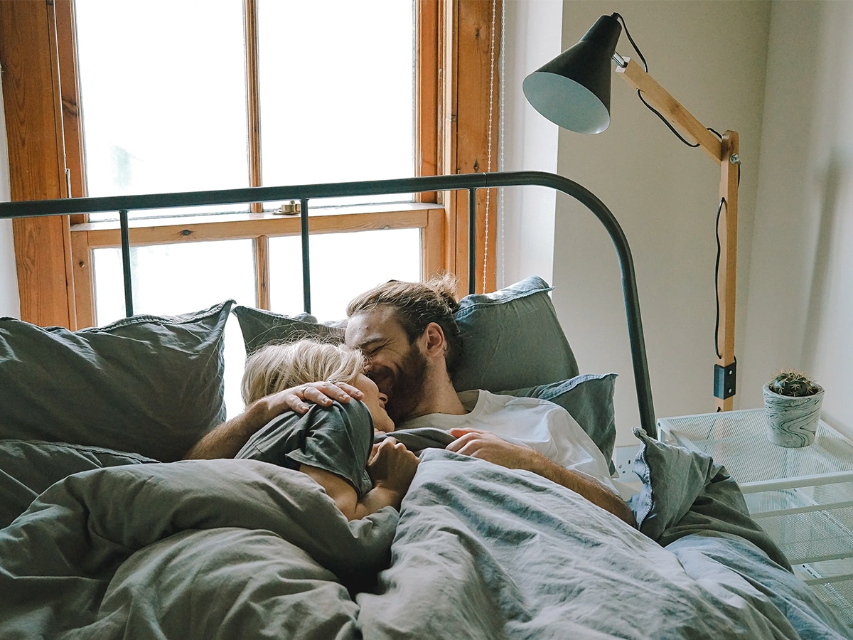 Man kissing woman on her forehead as they wake up from bed