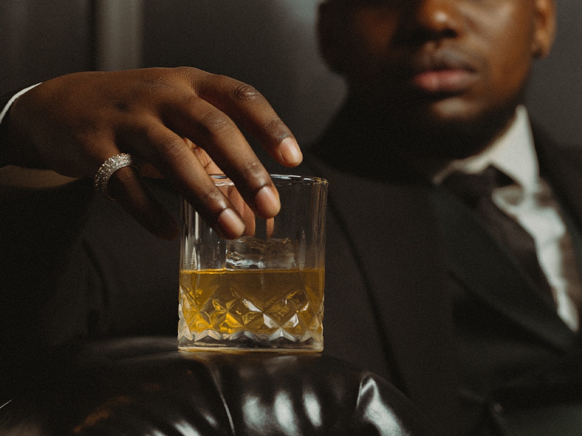 Close-up of a man placing a glass of whisky on a leather couch arm rest