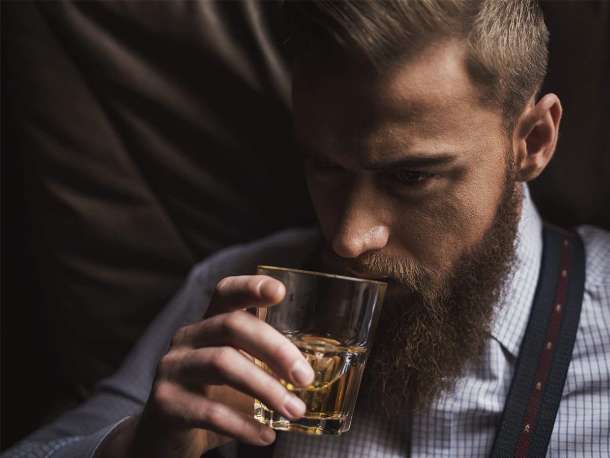 Close-up of a man’s face holding a glass of whisky near his nose