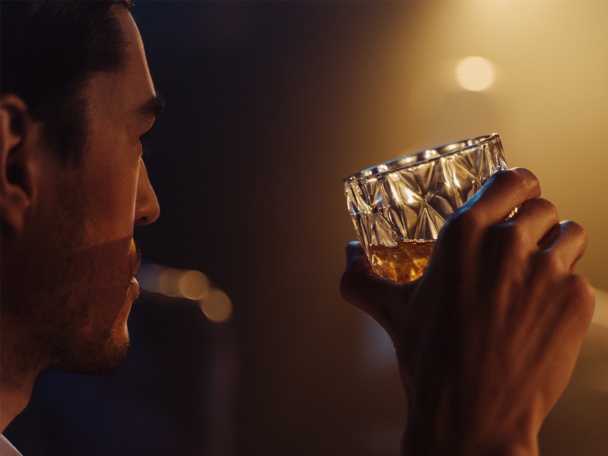 Close-up of a man’s face and hand swirling a glass of whisky