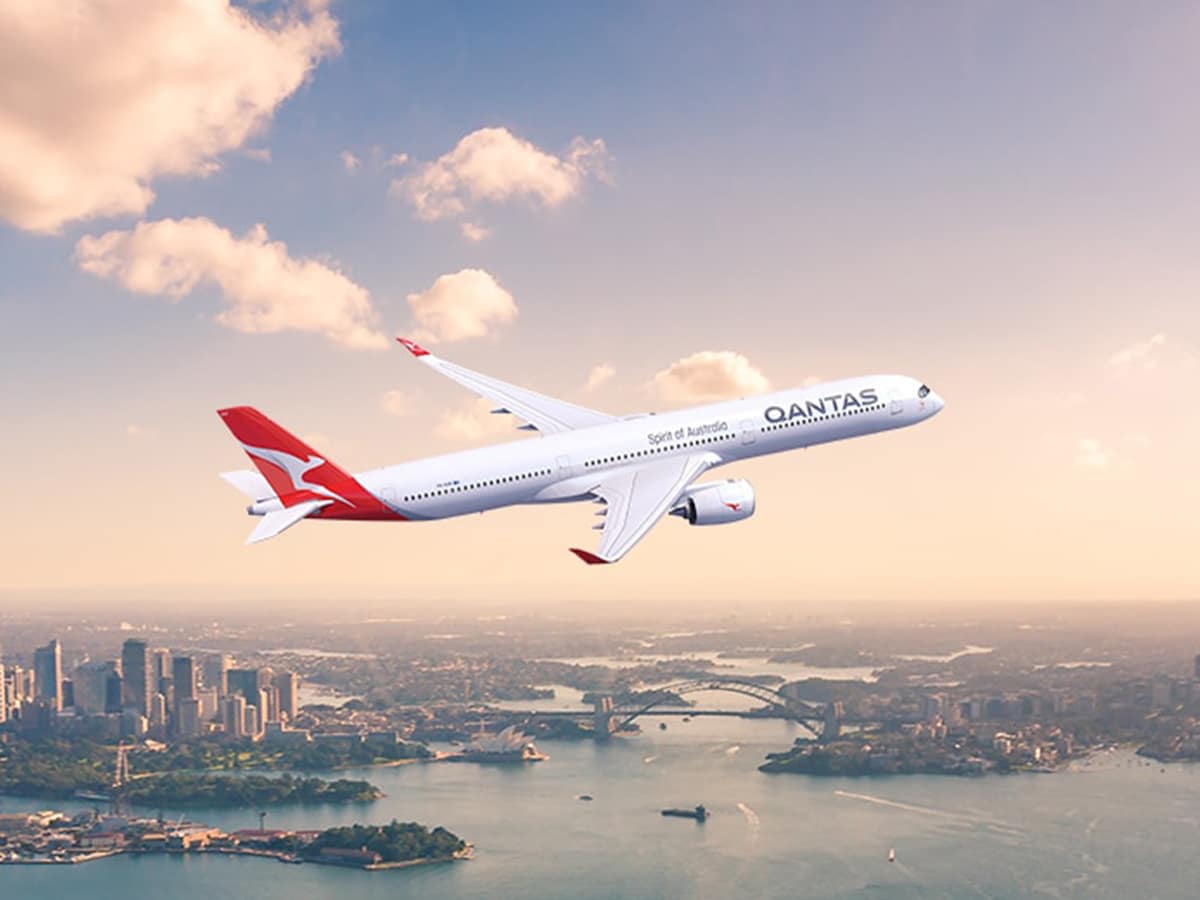 Qantas A350 flying over Sydney Harbour with city skyline and Harbour Bridge in the background.