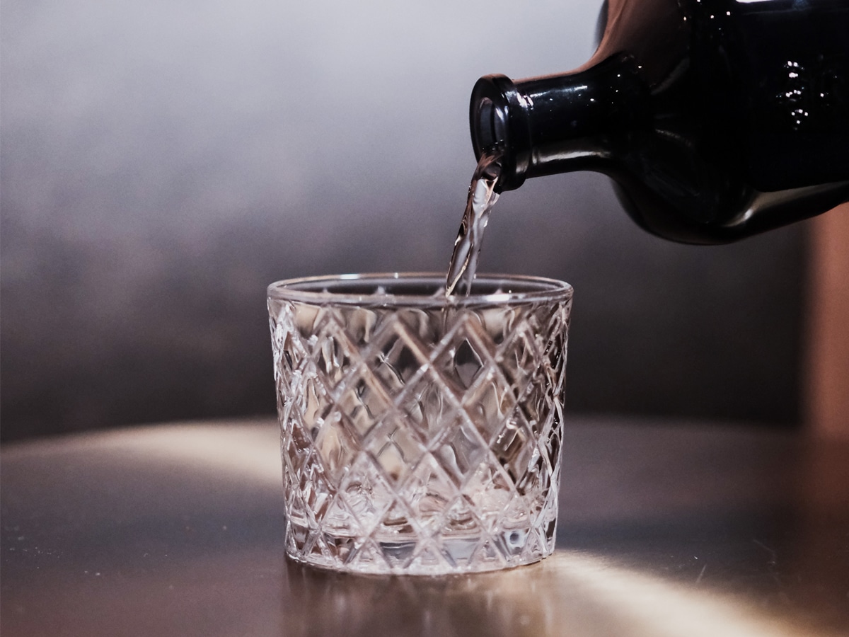 A clear glass being filled with mezcal from a black bottle