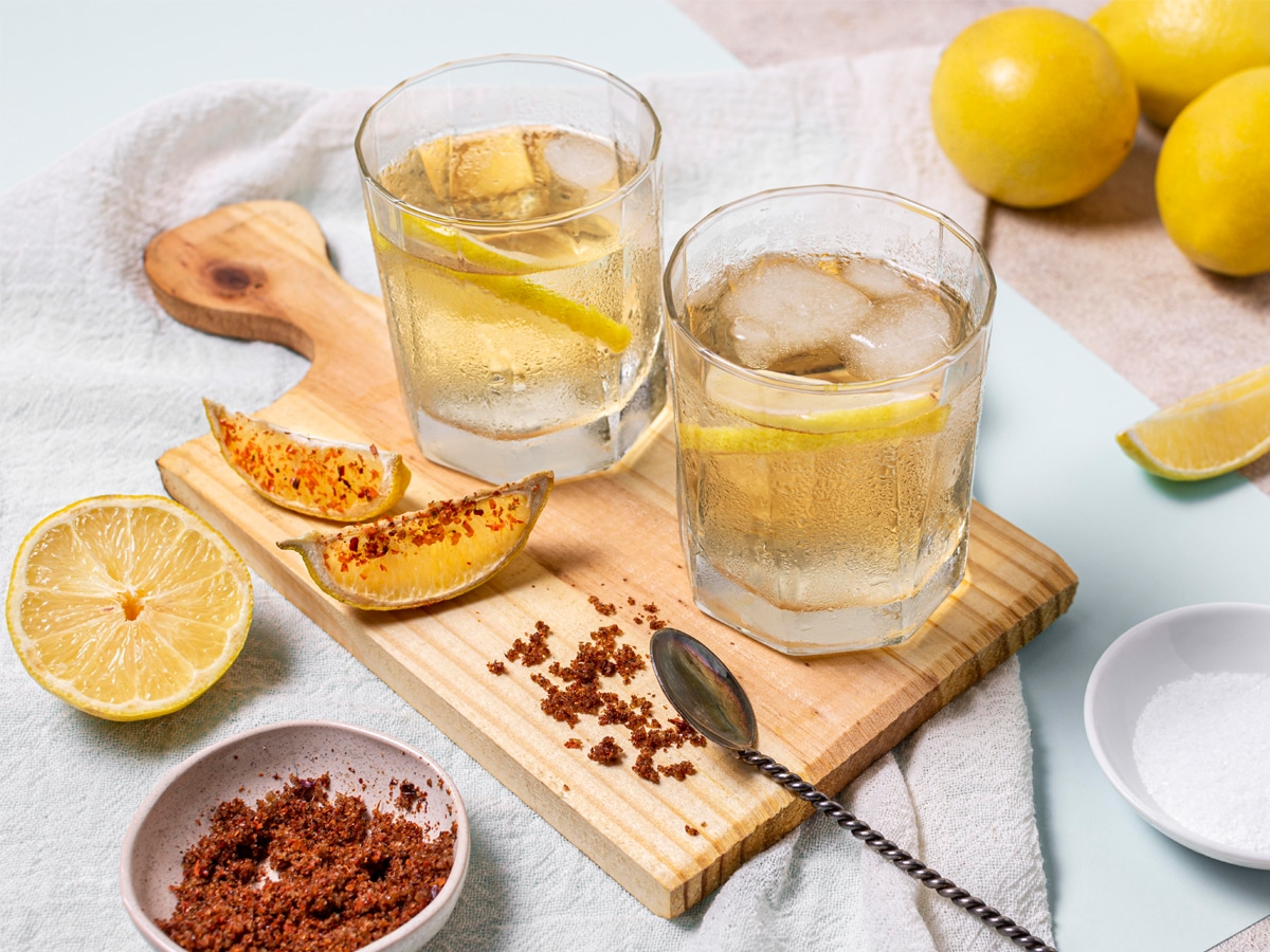 A pair of crystal-clear glasses filled with mezcal and ice cubes with lemon slices