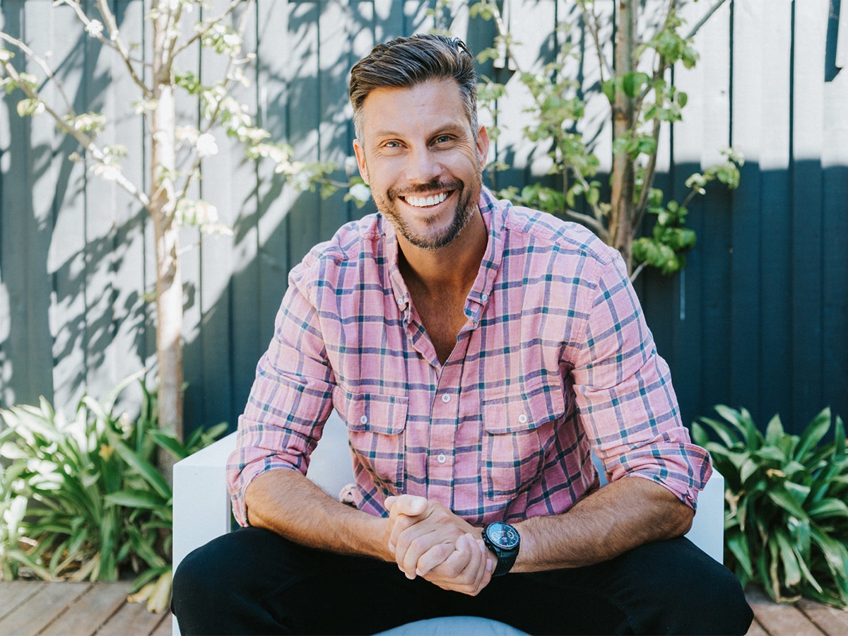 Sam Wood sitting outdoor and smiling with clasped hands