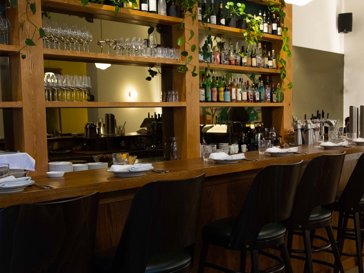 Interior of Alta Trattoria restaurant showing bar area with black chairs and liquor bottle display