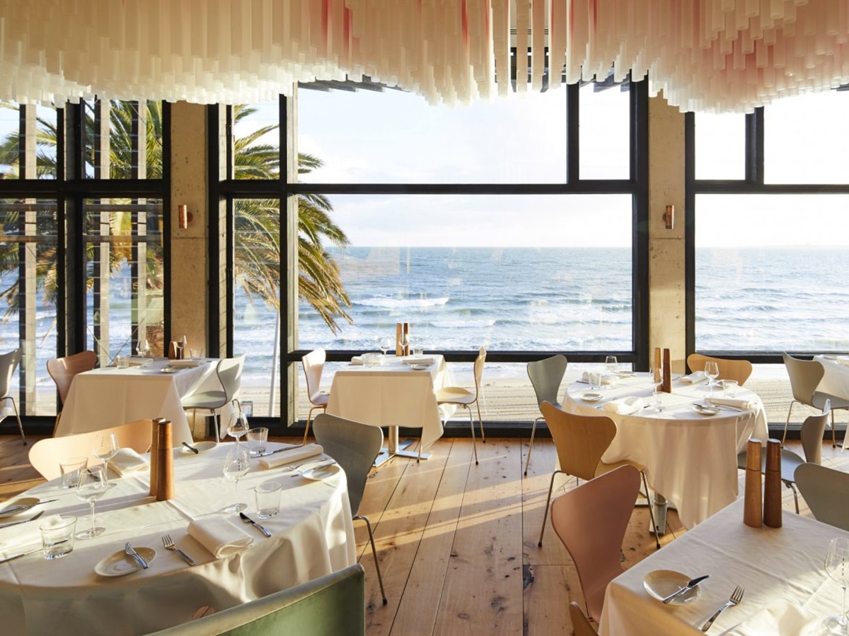 Interior of Stokehouse restaurant with cream and green colour scheme showing tables, chairs and wide glass windows overlooking the beach