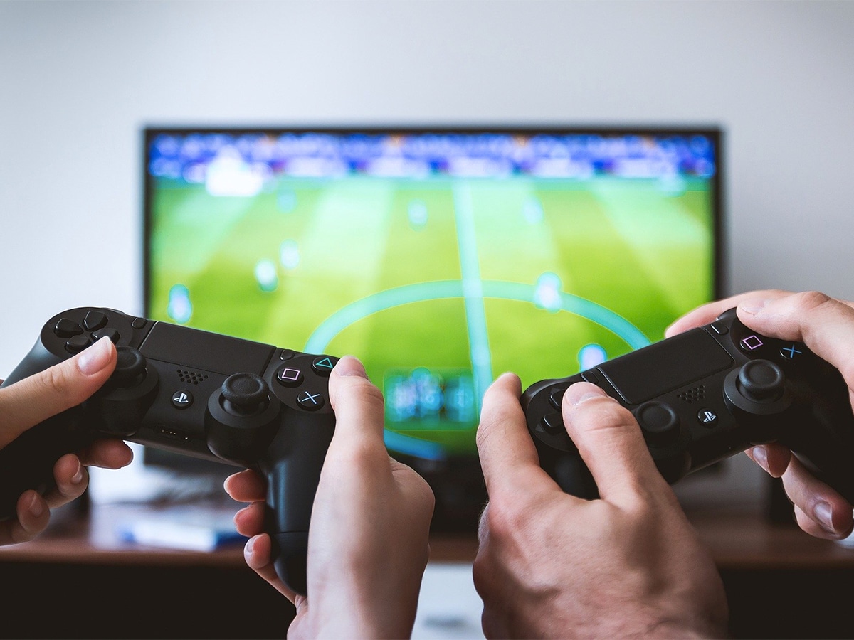 Close up of couple’s hands holding their game controllers with the game displayed on a screen in the background