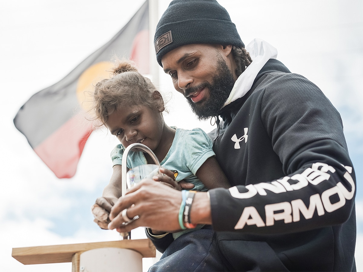 Patty Mills helping a child reach the faucet to get drinking water