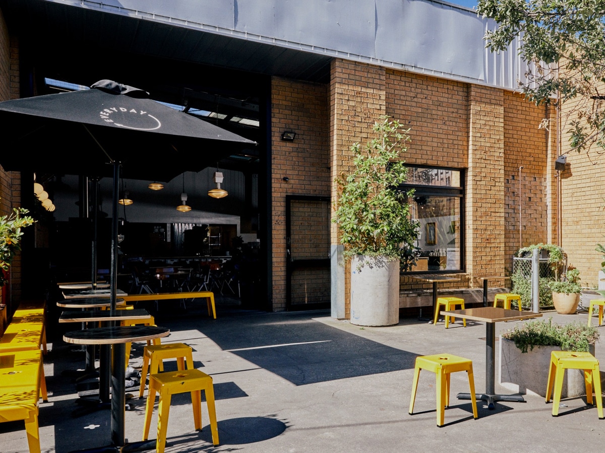 Exterior of Everyday Coffee cafe with black patio umbrellas, black tables and yellow chairs