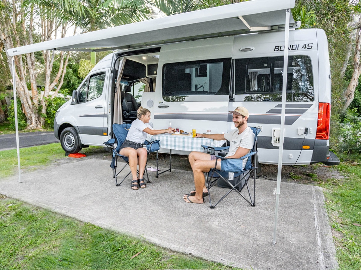 A couple enjoying a meal at a table in front of their Bondi campervan