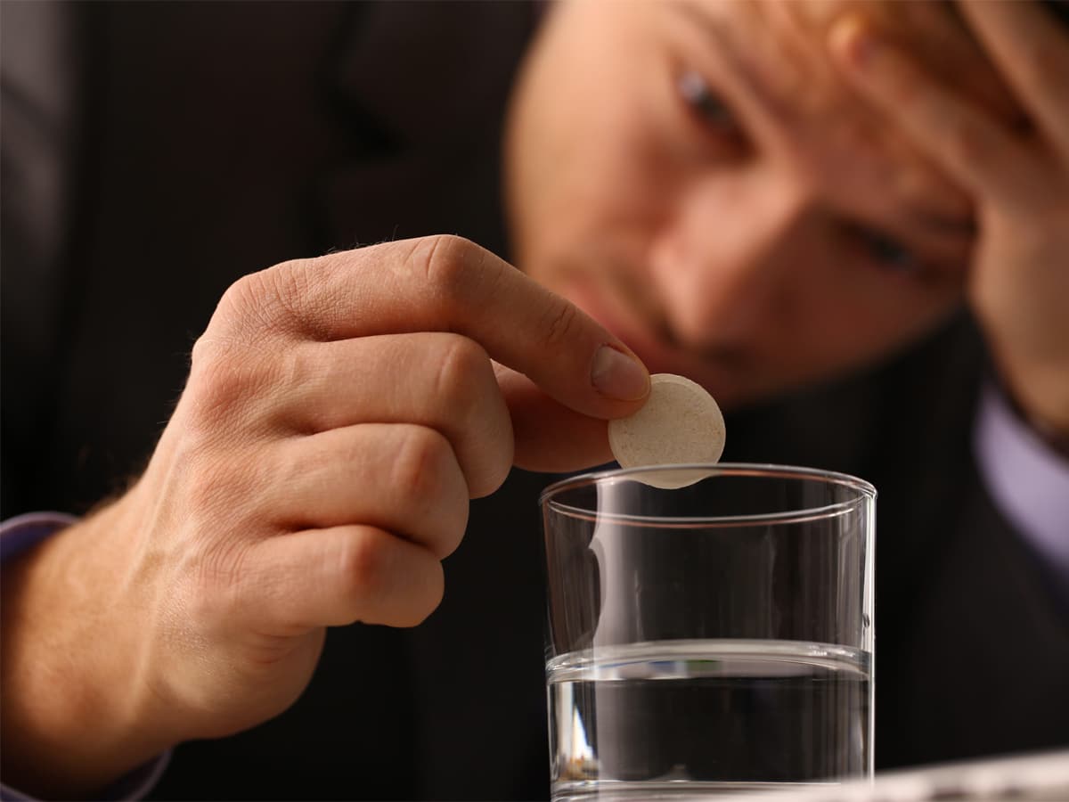 Close up of a man's hand about to drop a tablet on a glass of water