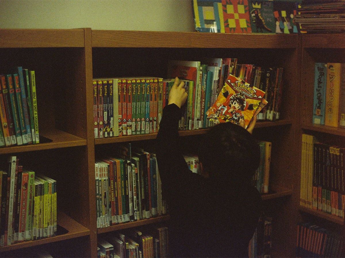 Person in black long sleeve shirt arranging comics near brown wooden shelf
