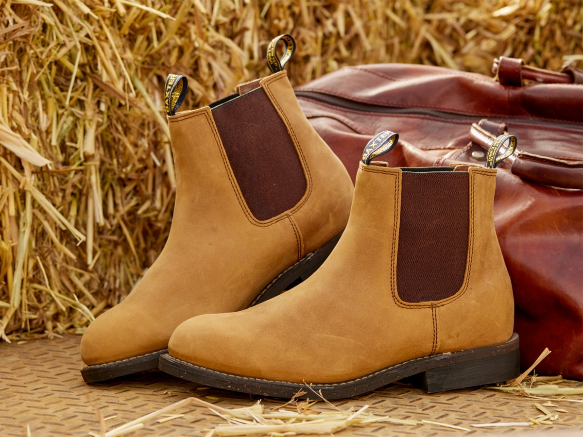 Pair of brown boots in front of a red bag and haystack