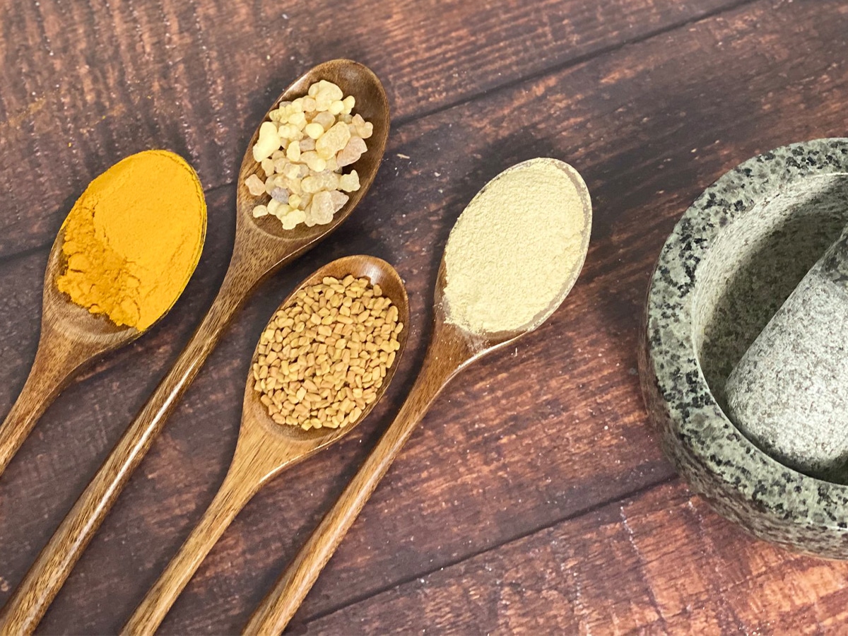Mortar and pestle beside Turmeric, Fenugreek, Boswellia and Ashwagandha on a wooden spoon