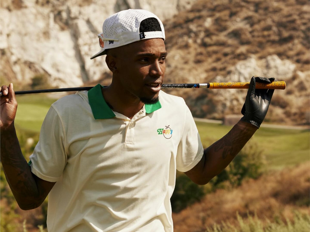 A golfer in a white and green shirt, black golf glove, and a white cap