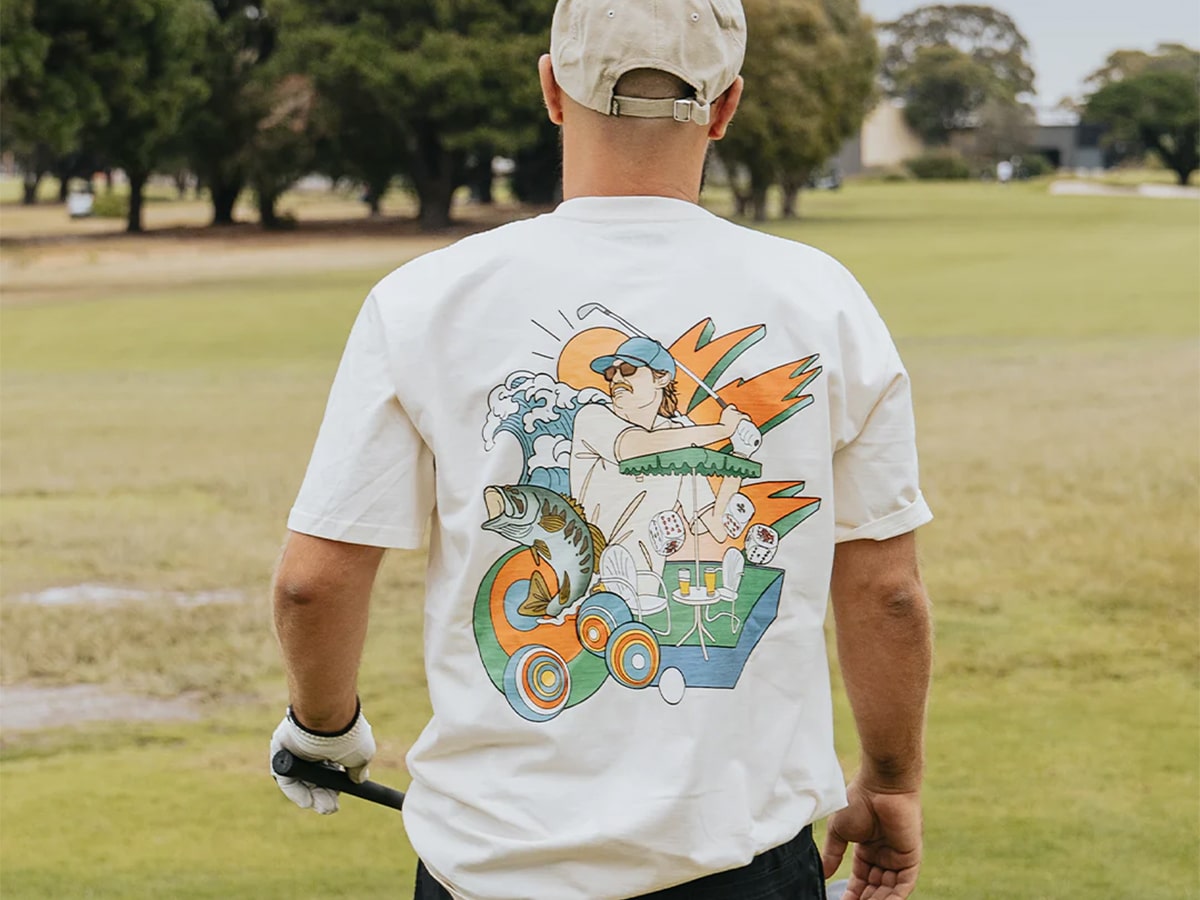 A golfer in a white graphic t-shirt, white golf glove, and khaki cap