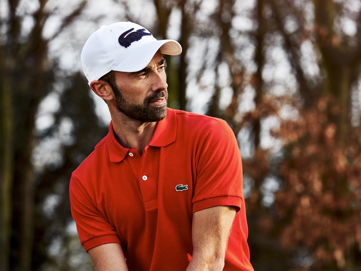 A golfer in a red Lacoste shirt wearing a white Lacoste cap