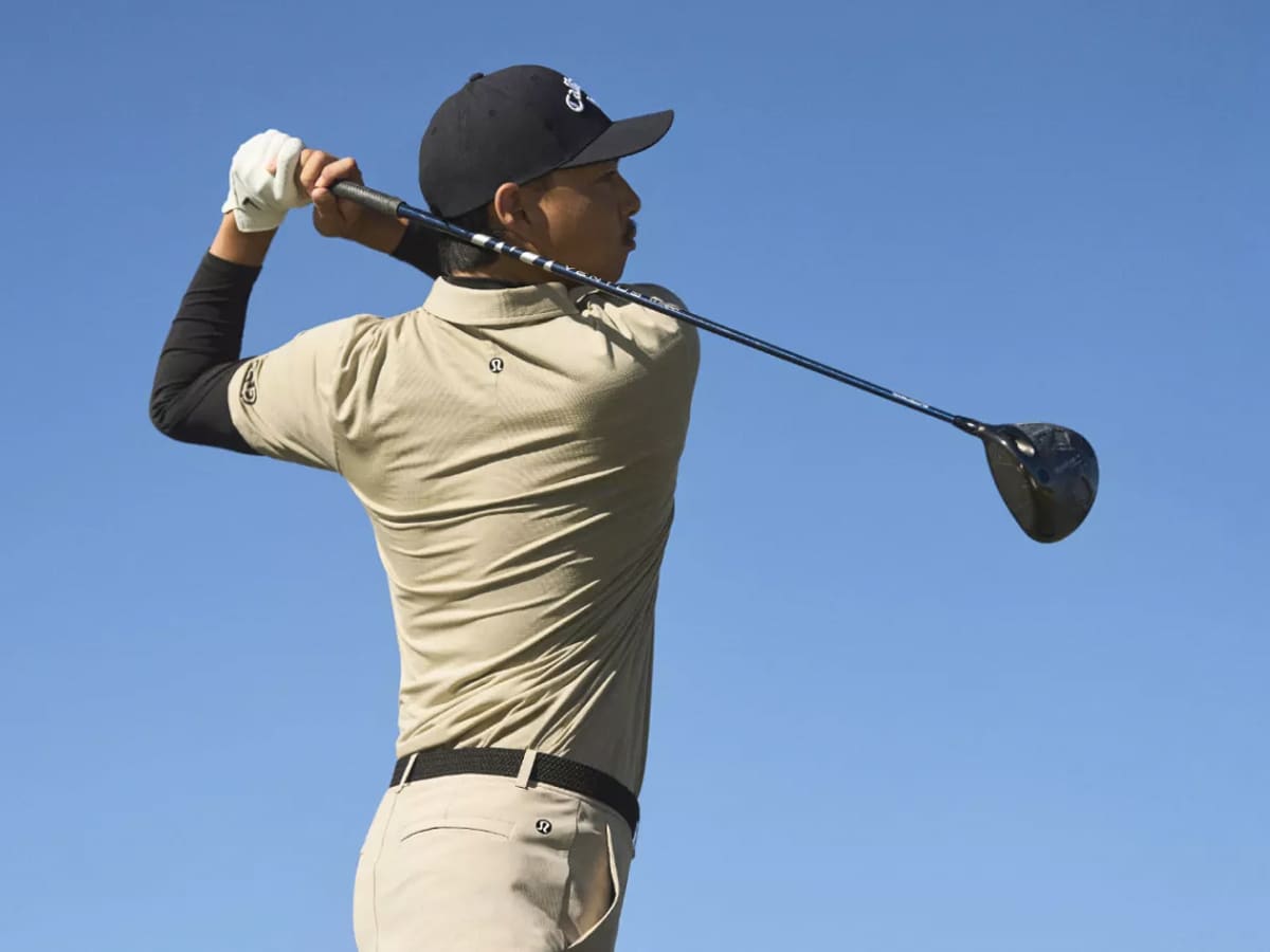 A golfer in an off white and black long sleeve shirt and a white golf glove and pants