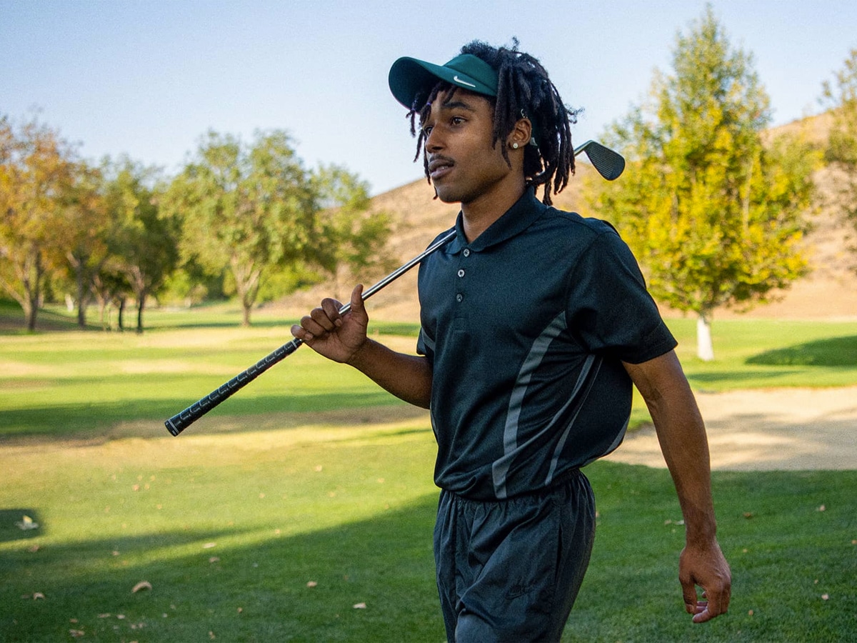 A golfer in a black shirt, pants, and visor
