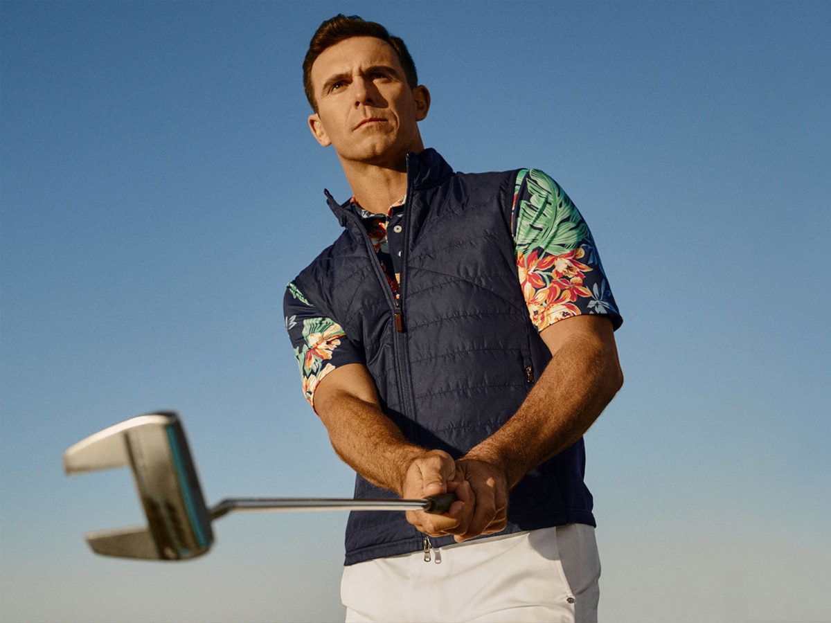 A golfer in a Hawaiian shirt underneath a black sleeveless jacket