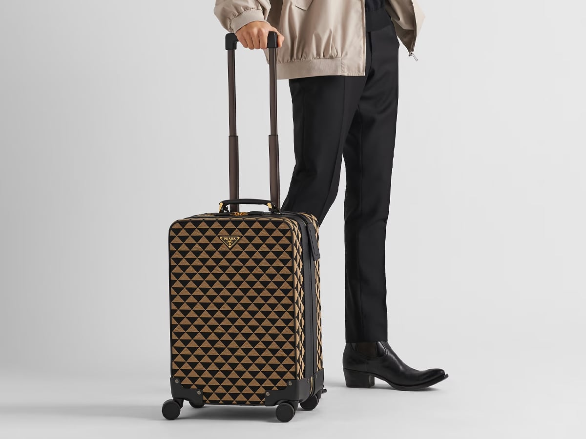 Male model holding Prada patterned luggage