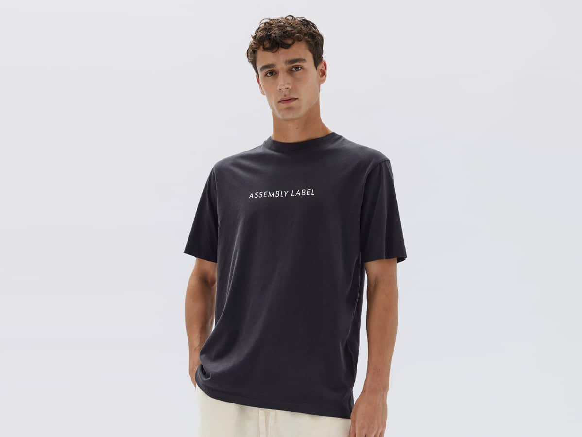 Male model wearing 'Assembly Label' printed plain black shirt