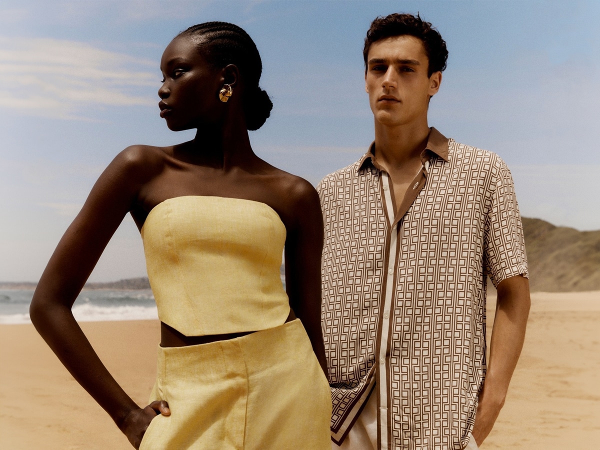Female model wearing matching yellow crop top and bottom set beside a male model wearing white and brown printed shirt