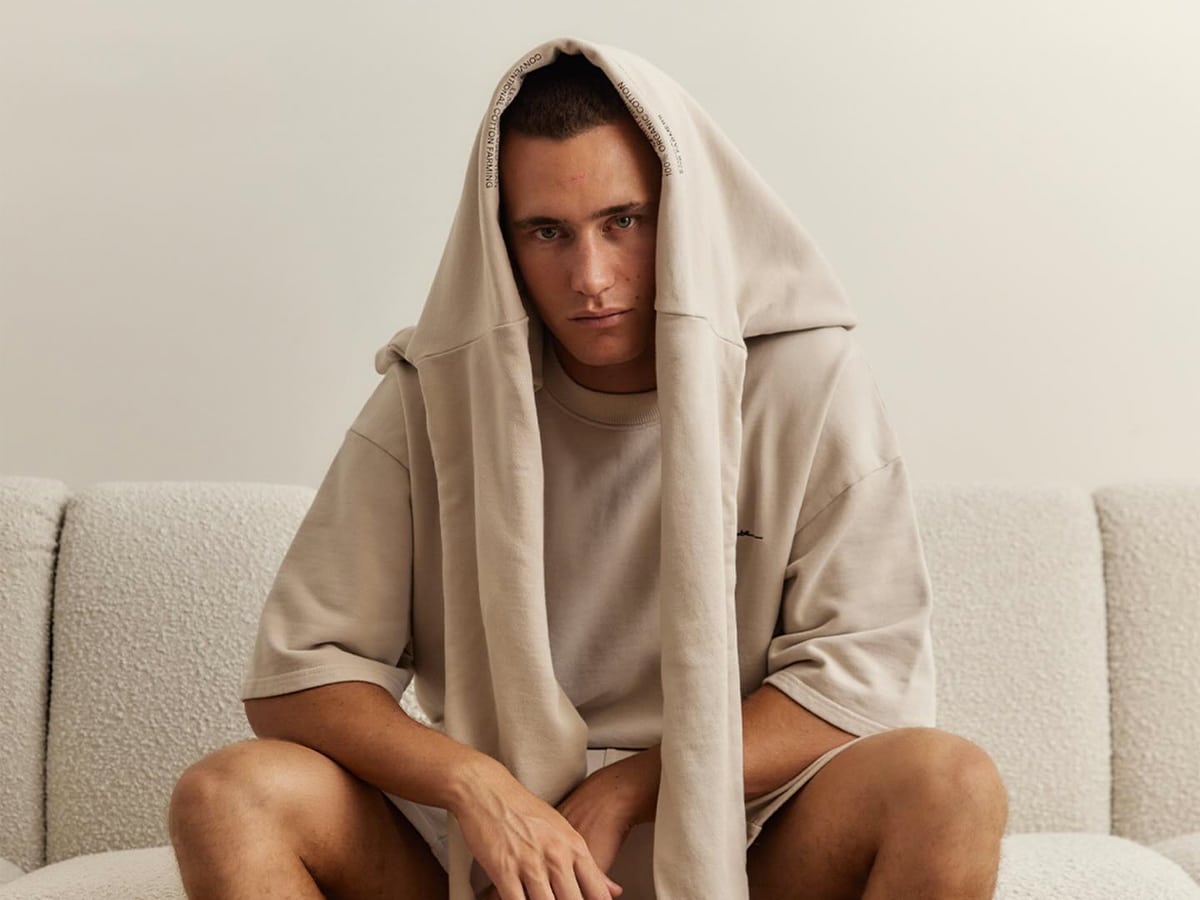 Male model wearing nude oversized shirt with a nude sweatshirt draped over his head