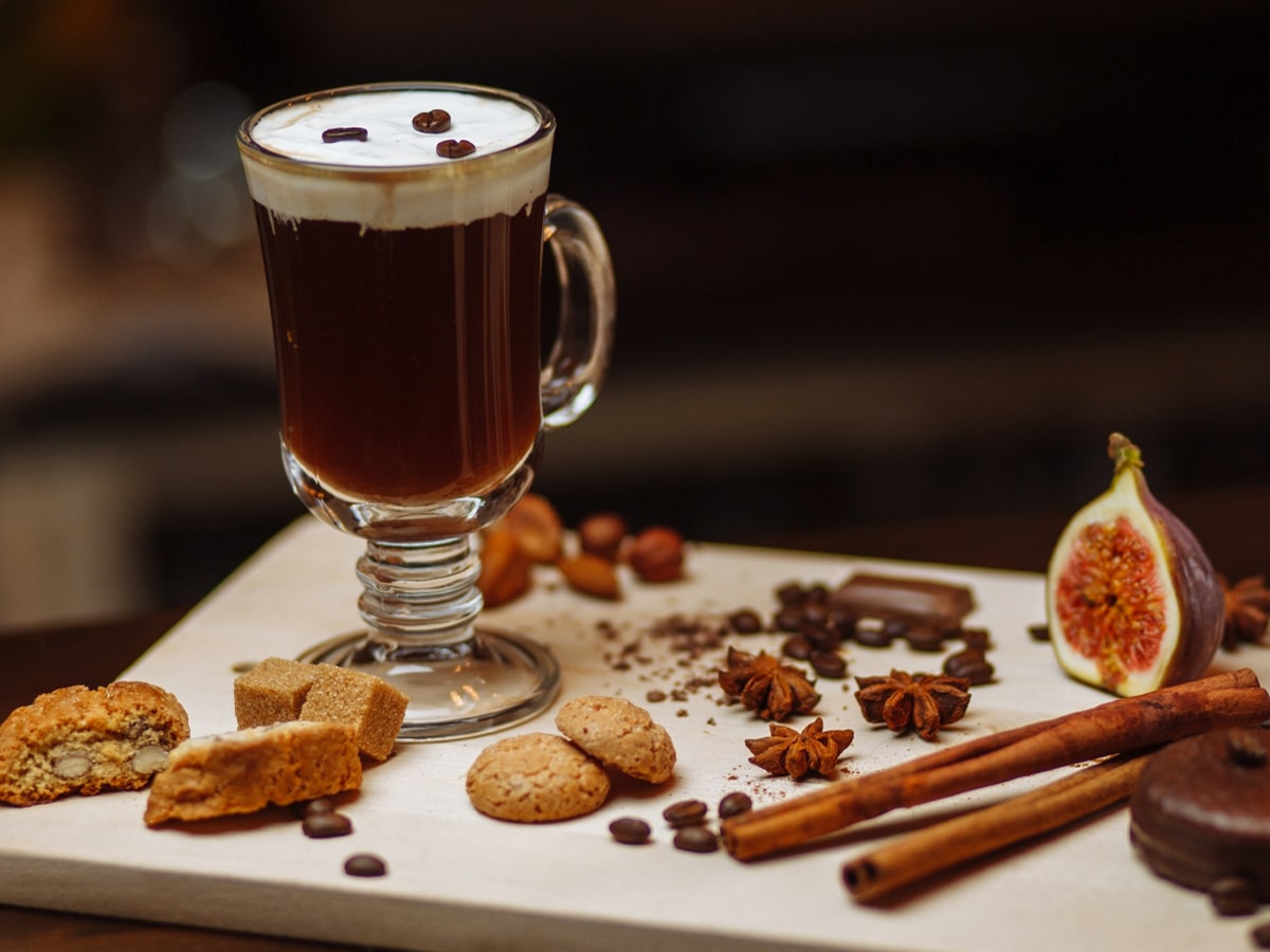 A mug of irish coffee set on a white bar with cookies, almonds, coffee beans