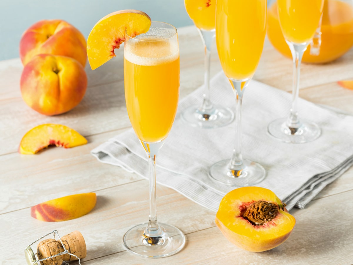 Glasses of peach bellini with peach garnish set on a wooden table