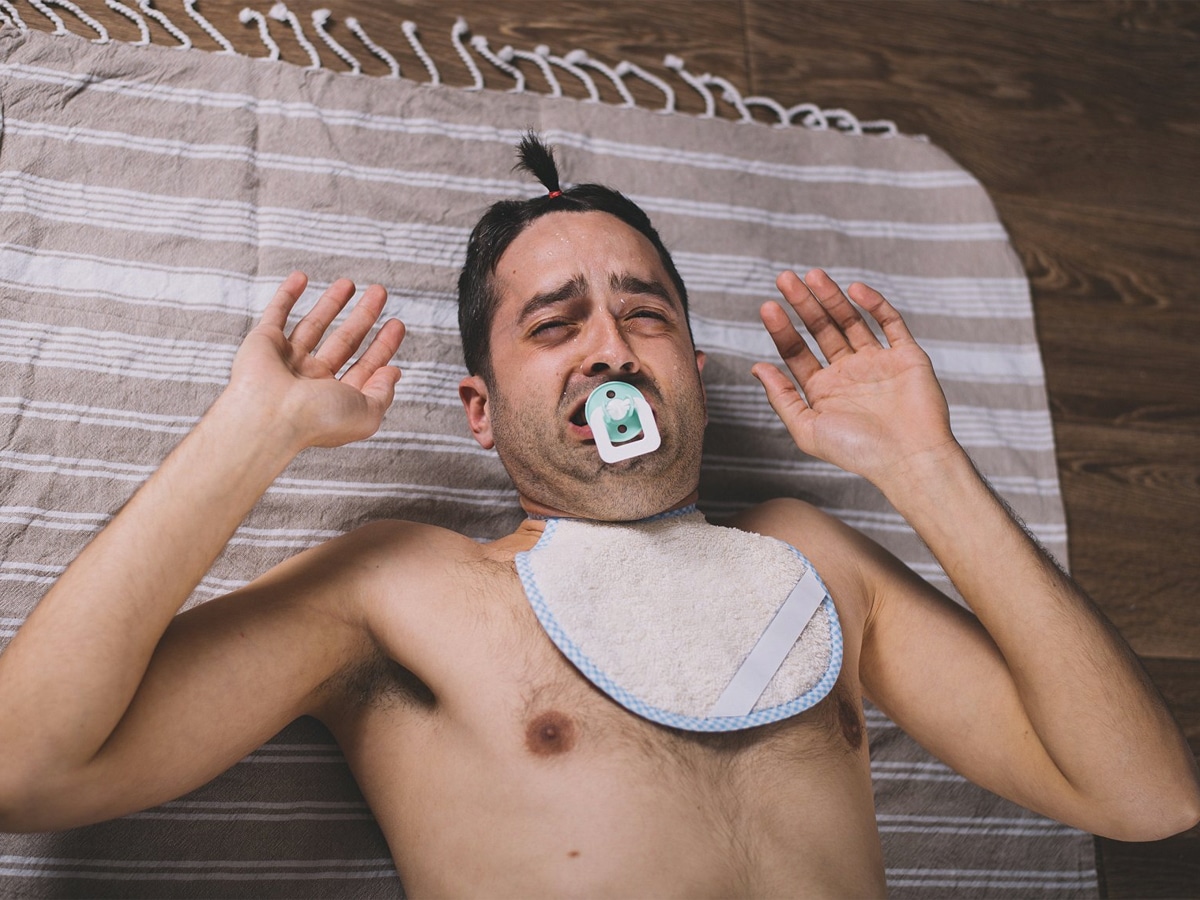 A man with a pacifier and bib pretending to be a baby