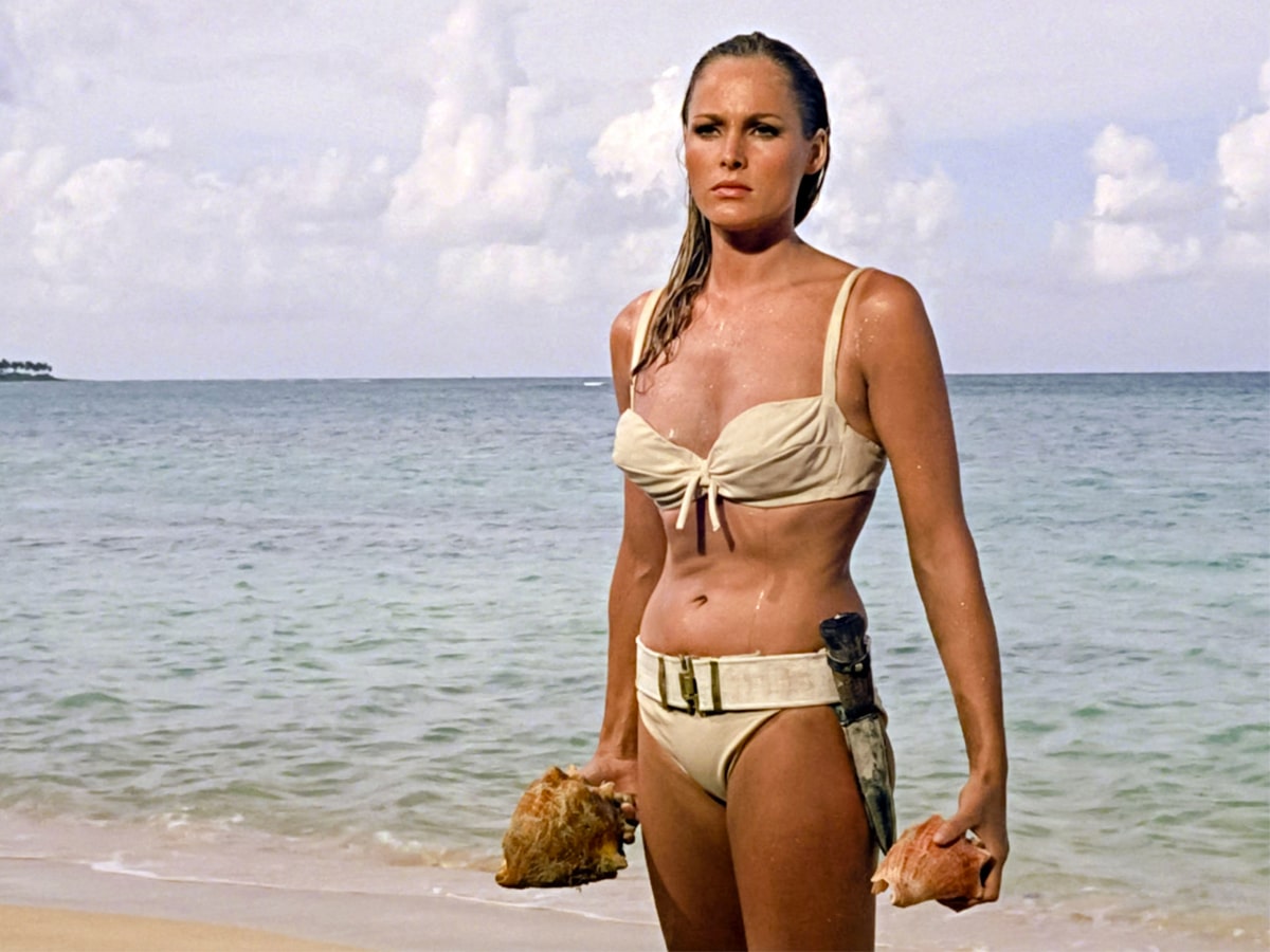 Ursula Andress in a swimsuit holding seashells by the beach