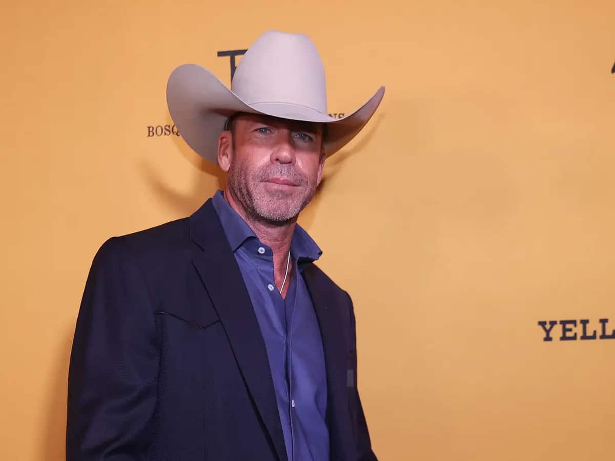 Man in a cowboy hat and suit jacket against a yellow background.