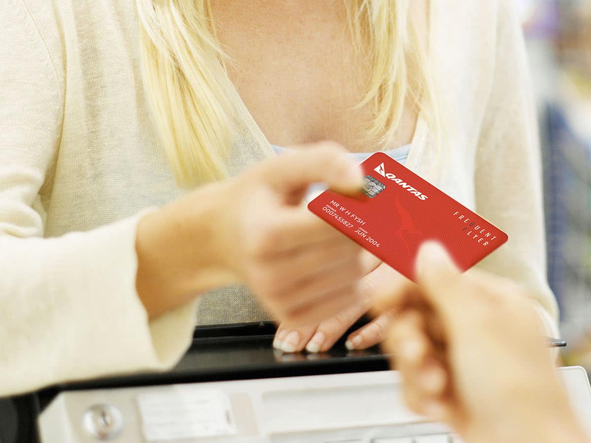 Woman handing Qantas Frequent Flyer card to cashier