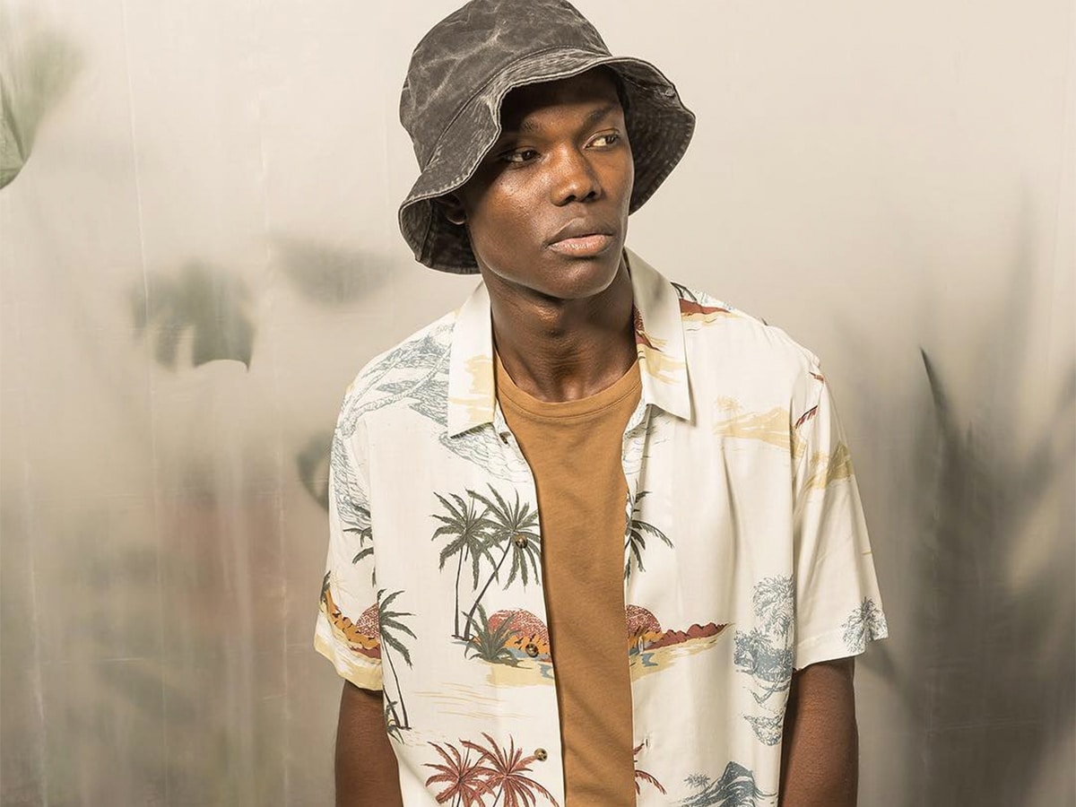 Male model in a brown t-shirt underneath tropical print shirt and a grey bucket hat