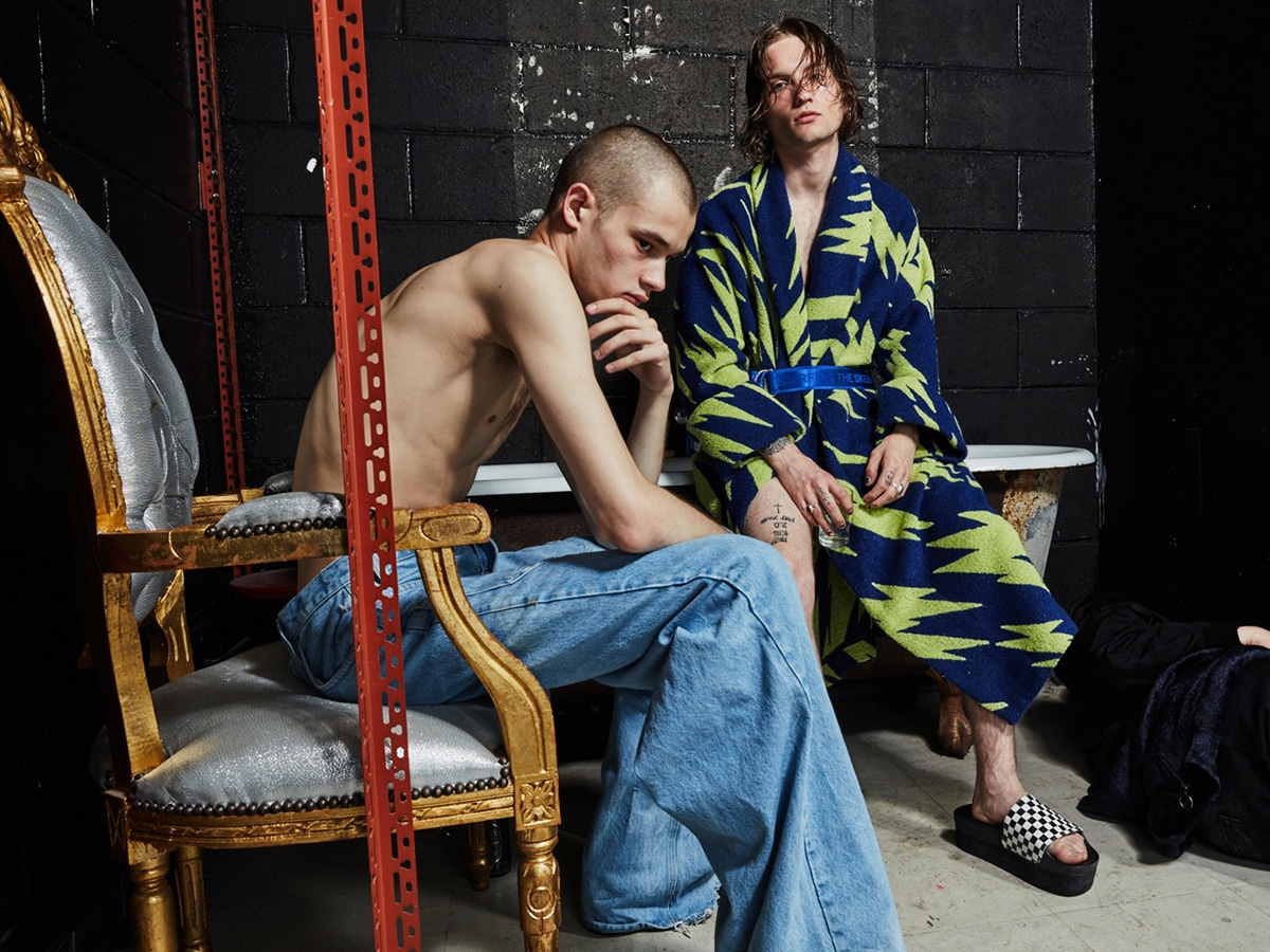 Male model in a a printed green and blue robe behind another male model in denim pants