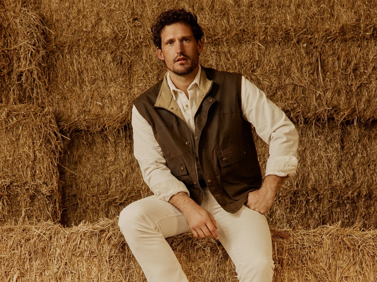 Male model in a beige long sleeve shirt underneath a brown gilet and beige pants