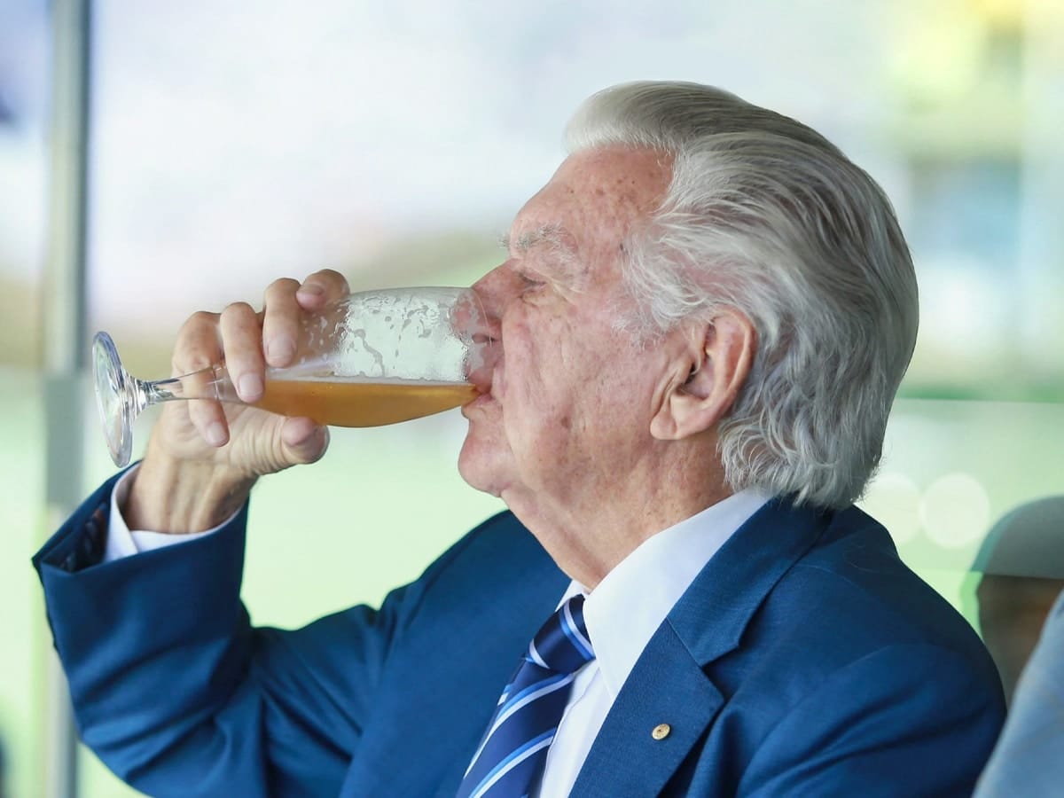 Old man in a blue suit drinking a glass of alcohol